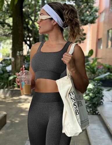 Woman in athletic wear holding iced coffee and tote bag outdoors.